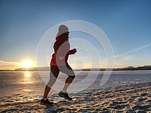 Woman running along shore of a frozen lake in winter spring