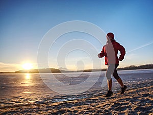 Woman running along shore of a frozen lake in winter spring
