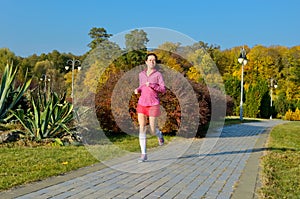 Woman running in autumn park, beautiful girl runner jogging