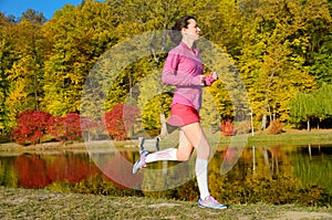 Woman running in autumn park, beautiful girl runner jogging