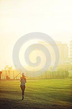 Woman, running and back on grass for exercise with mock up space in sky with buildings in city. Girl, person and athlete