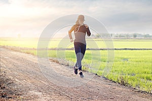 Woman running excercise on rural road of green field sunset