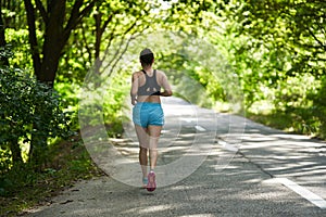 Woman running through forest on asphalt