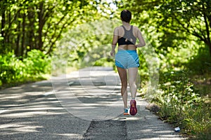 Woman running through forest on asphalt