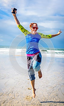 Woman running and jumping on beach with ocean in background