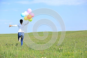 Woman running and jumping on green grassland with colored balloons