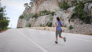 Woman running outdoors. Young energetic active woman in sportswear jogging on empty road in mountains. Female athlete exercising a