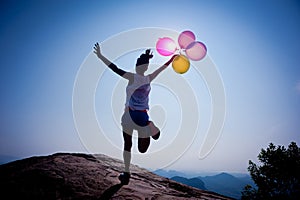 woman running on sunrise mountain top edge with balloons