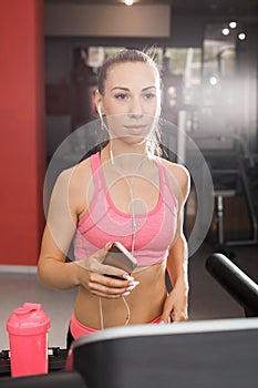 Woman running at the treadmill holding a phone