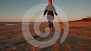 Woman running, walking, playing and having fun with her doggy at sunset on a beach near Baltic sea in spring. Colorful