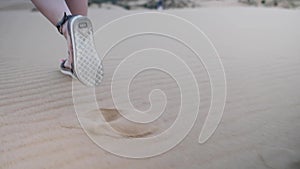 A woman runs barefoot on a sandy beach in slow motion in sandals.