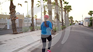 Woman runs down the street along the palm avenue at sunset. Healthy active lifestyle. Back view