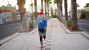 Woman runs down the street along the palm avenue at sunset. Healthy active lifestyle. Slow motion