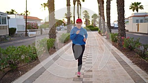 Woman runs down the street along the palm avenue at sunset. Healthy active lifestyle. Slow motion