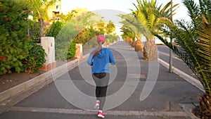 Woman runs down the street among the palm trees at sunset, back view. Healthy active lifestyle