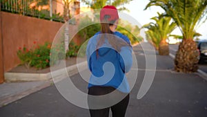 Woman runs down the street among the palm trees at sunset, back view. Healthy active lifestyle