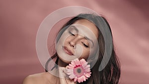 A woman runs a gerbera flower across her perfect skin. Portrait of a woman with a gerbera flower in the studio on a pink