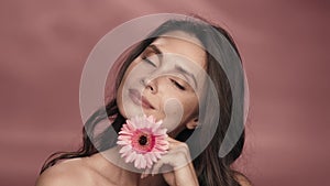 A woman runs a gerbera flower across her perfect skin. Portrait of a woman with a gerbera flower in the studio on a pink