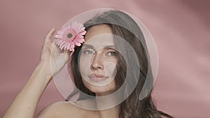 A woman runs a gerbera flower across her perfect skin. Portrait of a woman with a gerbera flower in the studio on a pink