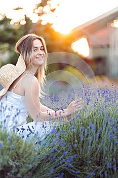 Woman runs her hand over lavender bush. girl with cute smile walks in evening in lavender meadow