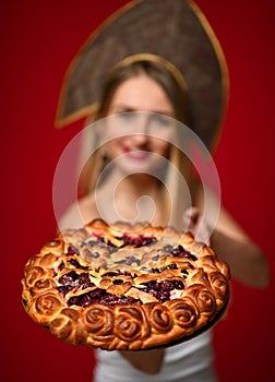 Woman in Russian traditional cap hat kokoshnik happy smiling hold sweet cherry homemade pie tasty bun
