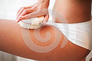 Woman`s arm holding dry brush to top of her leg. Cellulite treatment, dry brushing