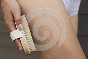 Woman`s arm holding dry brush to top of her leg. Cellulite treat