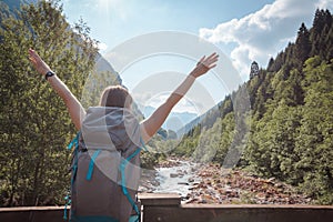 Woman`s arms raised on a bridge crossing a river surrounded by mountains