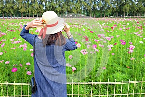 Woman`s back wearing straw hat while looking at flower garden.