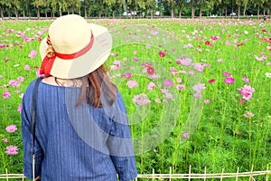 Woman`s back wearing straw hat while looking at flower garden.