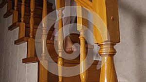 A woman's bare feet in gray pants descend the oak stairs. View from the side over the railing.