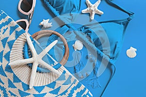 Woman`s beach accessories: bikini, bag, sunglasses, earrings, starfish and shells on bright blue background. Summer creative