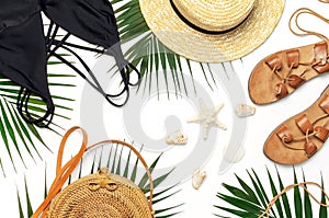 Woman`s beach accessories flat lay. Round trendy rattan bag straw hat black swimsuit leather sandals tropical palm leaves