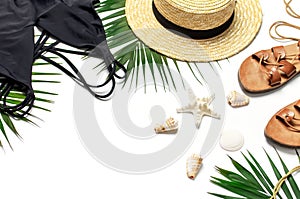 Woman`s beach accessories flat lay. Round trendy rattan bag straw hat black swimsuit leather sandals tropical palm leaves