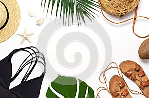 Woman`s beach accessories flat lay. Round trendy rattan bag straw hat black swimsuit leather sandals tropical palm leaves coconut