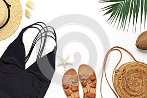 Woman`s beach accessories flat lay. Round trendy rattan bag straw hat black swimsuit leather sandals tropical palm leaves coconut