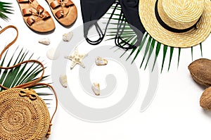 Woman`s beach accessories flat lay. Round trendy rattan bag straw hat black swimsuit leather sandals tropical palm leaves coconut