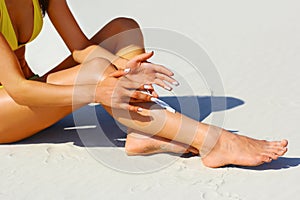 Woman`s beautiful legs on the beach. Tan Woman Applying Sunscreen on Legs. Close-up