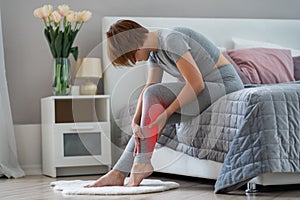 The woman`s calf muscle cramped, massage of female leg in home interior photo