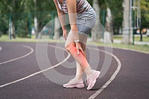 The woman's calf muscle cramped, massage of female leg on a sports ground after workout