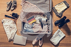 Woman`s clothes, laptop, camer and flag of Germany lying on the parquet floor near and in the open suitcase. Travel concept. photo