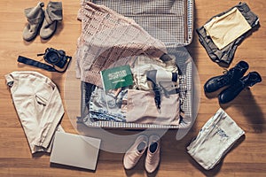 Woman`s clothes, laptop, camer and flag of Saudi Arabia lying on the parquet floor near and in the open suitcase. Travel