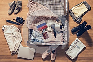 Woman`s clothes, laptop, camera, russian pasport and flag lying on the parquet floor near and in the open suitcase. Travel concep photo