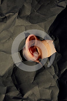 Woman`s ear in hole in black crumpled paper background, black and white concept photography for blog or poster