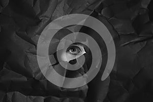 Woman`s eye in hole in black crumpled paper background, black and white concept photography for blog or poster