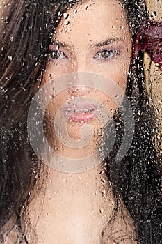 Woman's face behind glass full of water drops