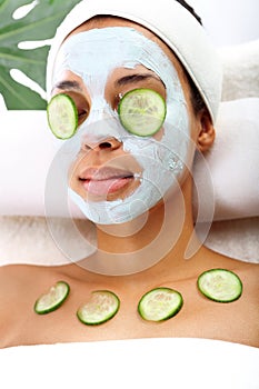 Woman's face in the mask mitigating and cucumber slices on eyes