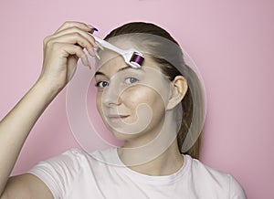 A woman`s face on a pink background with a mesoroller. Facial skin care. Moisturizing, anti-aging care