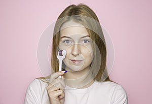 A woman`s face on a pink background with a mesoroller. Facial skin care. Moisturizing, anti-aging care