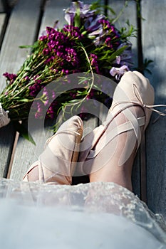 Woman`s feet in ballet slippers with lace hem and a nearby bouquet of wildflowers.